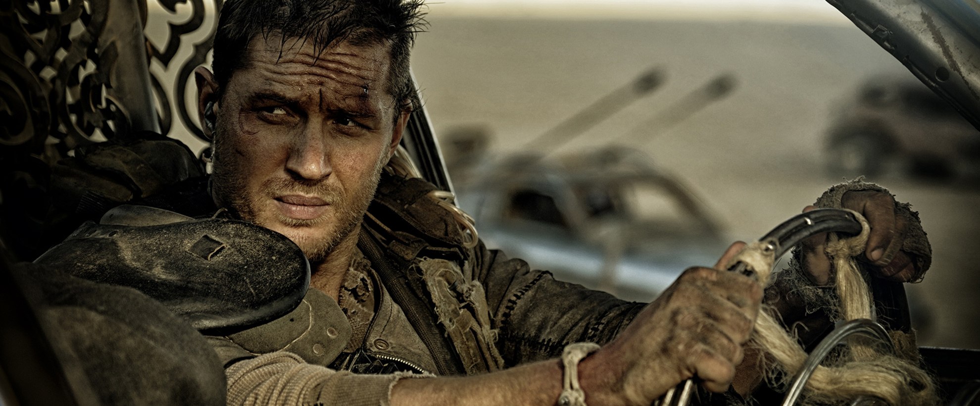 Tom Hardy as Mad Max, sitting in a car holding the steering wheel