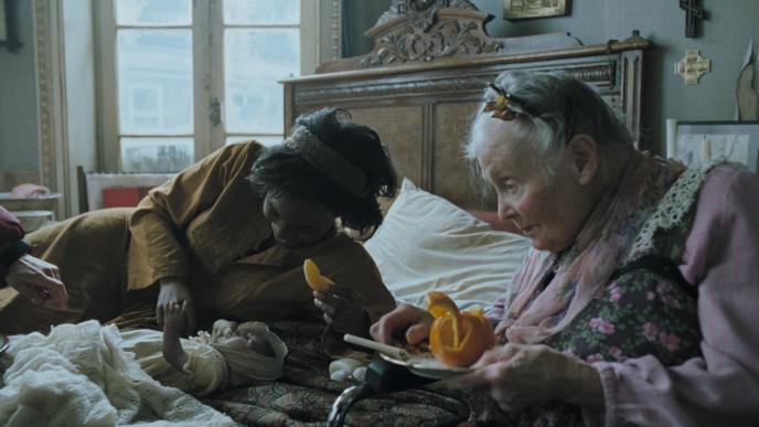 actress julianne moore from children of men laying on a bed with the baby and a grandmother holds a plate of eaten orange peels