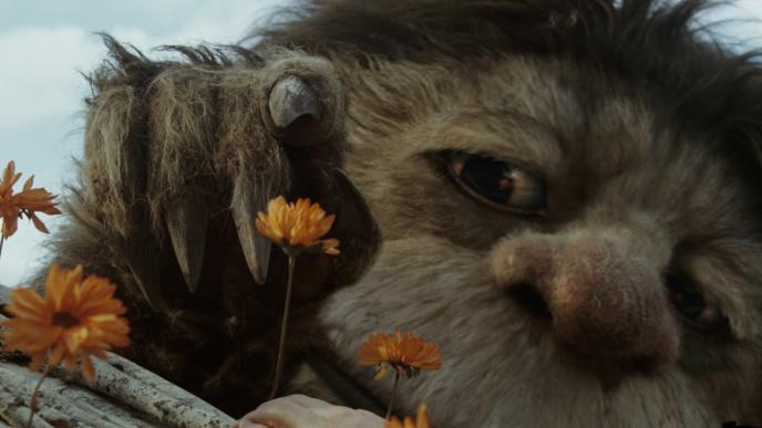 face close up of carol the monster from where the wild things are picking orange flowers