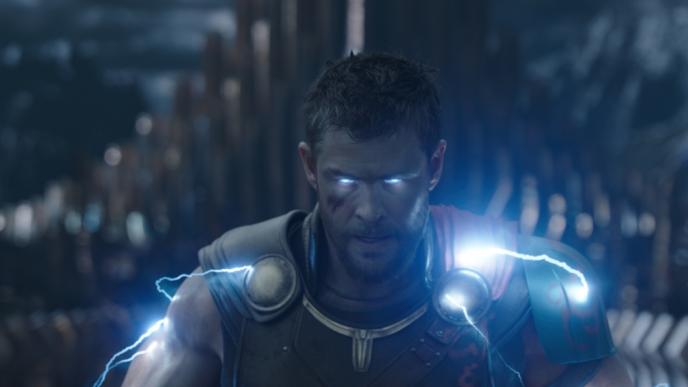 actor chris hemsworth as thor looking directly into the camera with lit up eyes and electric bolts sizzling around his shoulders