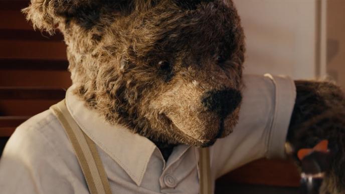 A human sized teddy bear wears a hat and button up shirt
