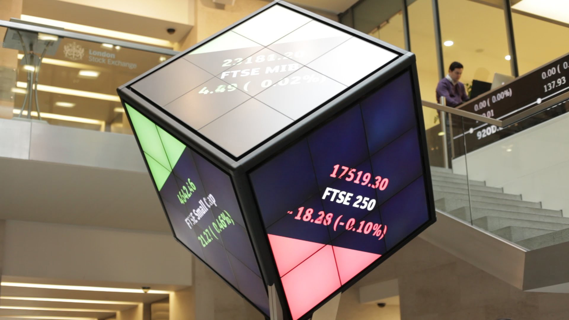 a cube screen suspended in air with the stock exchange projected on the screen