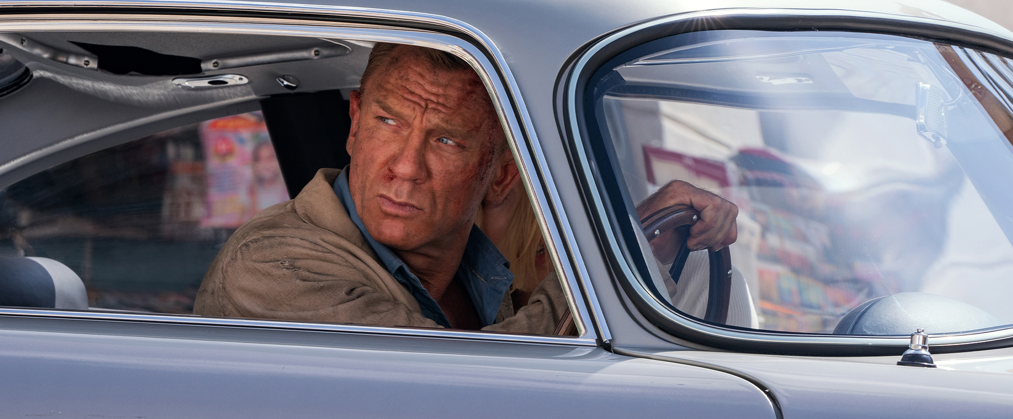 Daniel Craig as James Bond, driving a light blue vintage car