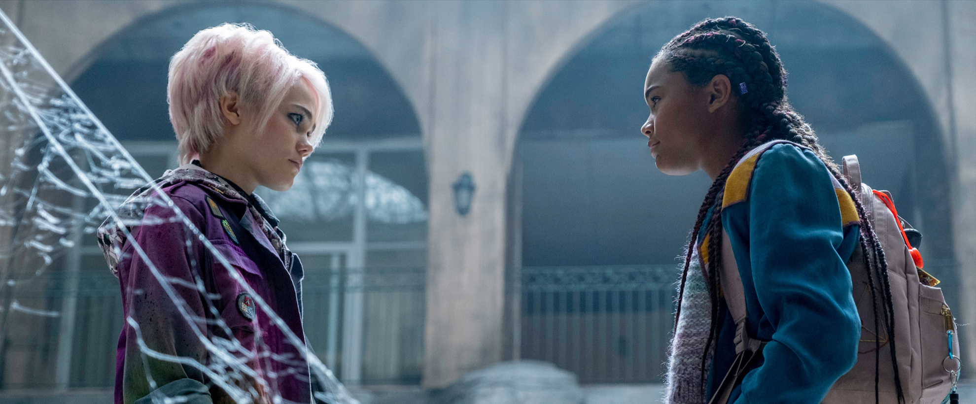 Two young girls stand facing each other, with cobwebs on the left hand side of the image