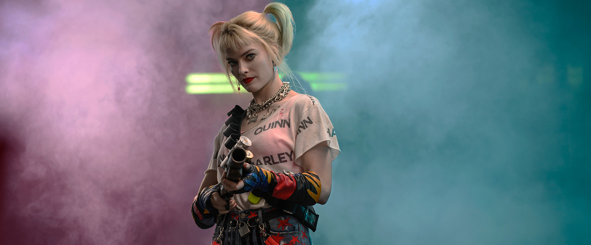 Margot Robbie as Harley Quinn, pointing a gun down the camera with pink and blue smoke in the background