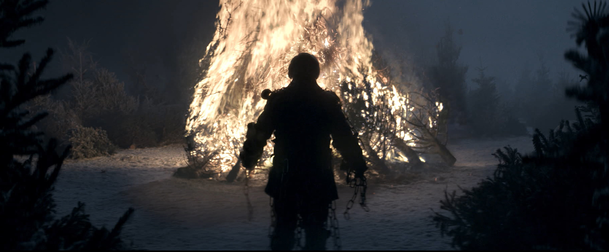 A raggedy silhouette of a man in front of a large bonfire