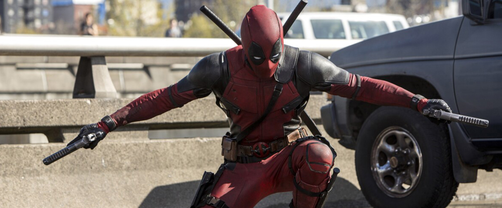 Deadpool lands in a crouch, wielding two guns