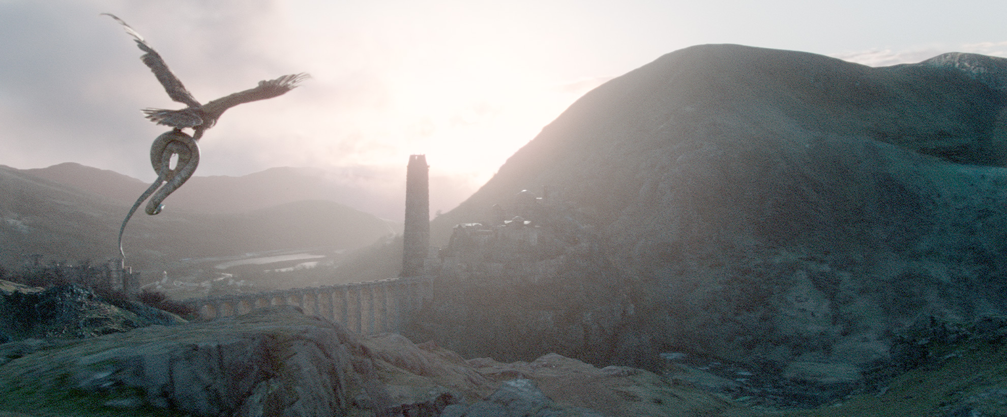 back view of an eagle soaring in the air over a bridge across mountainous terrain while holding a python snake