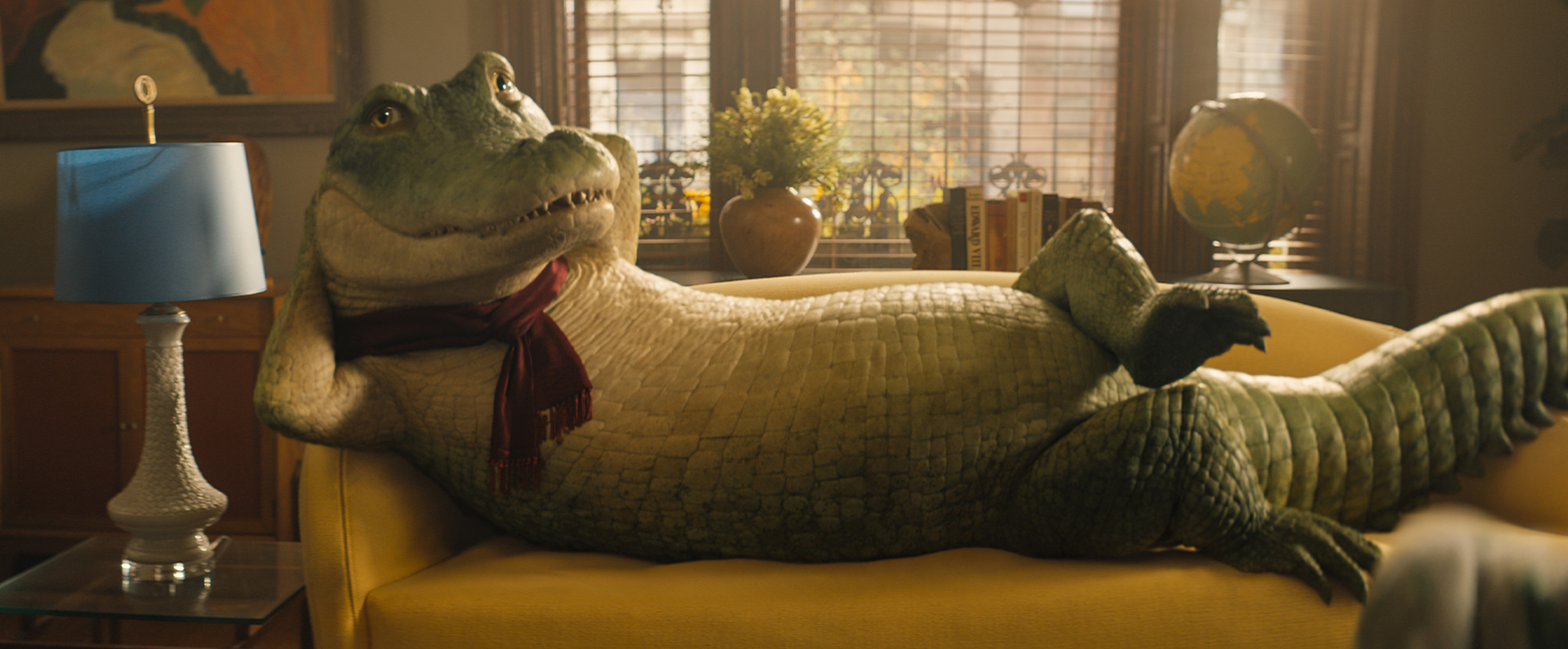 Lyle the crocodile, wearing a scarf, lying on a yellow couch