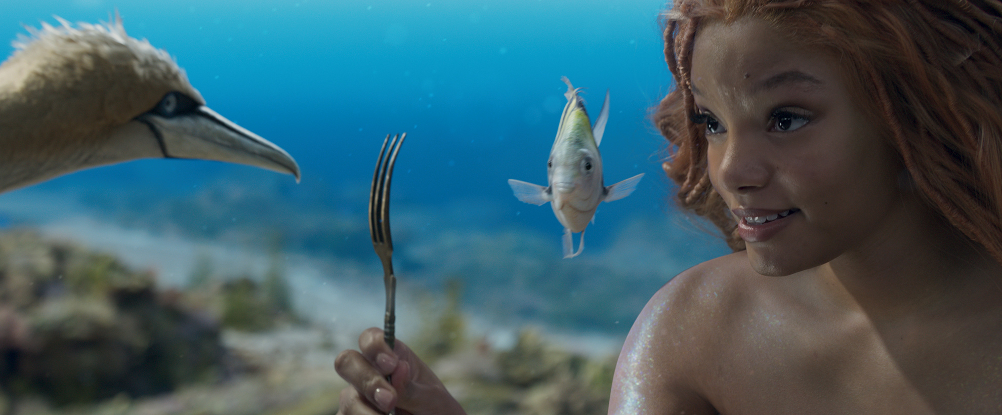 Halle Bailey as Ariel, holds a fork up to Scuttle and Flounder