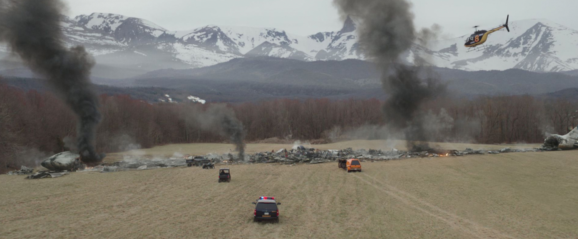 cars drive across a field to a mountain woodland, which is smoking