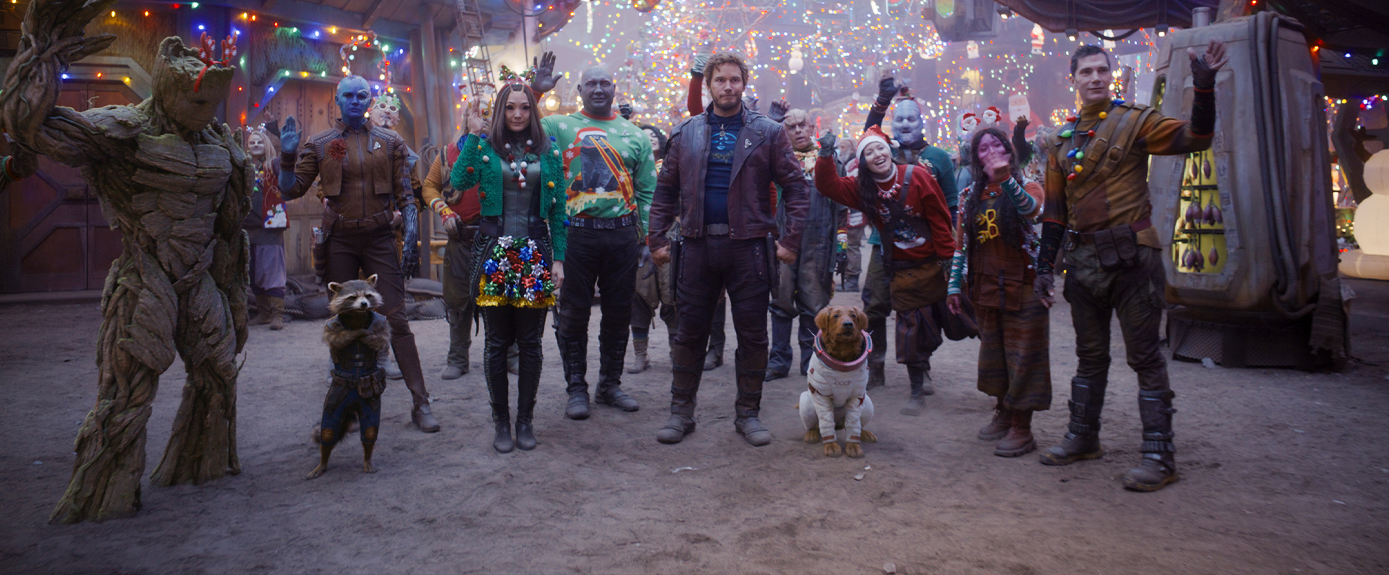 The cast of the Guardians of the Galaxy Holiday Special stand in Knowhere, decorated for Christmas, waving to someone off camera