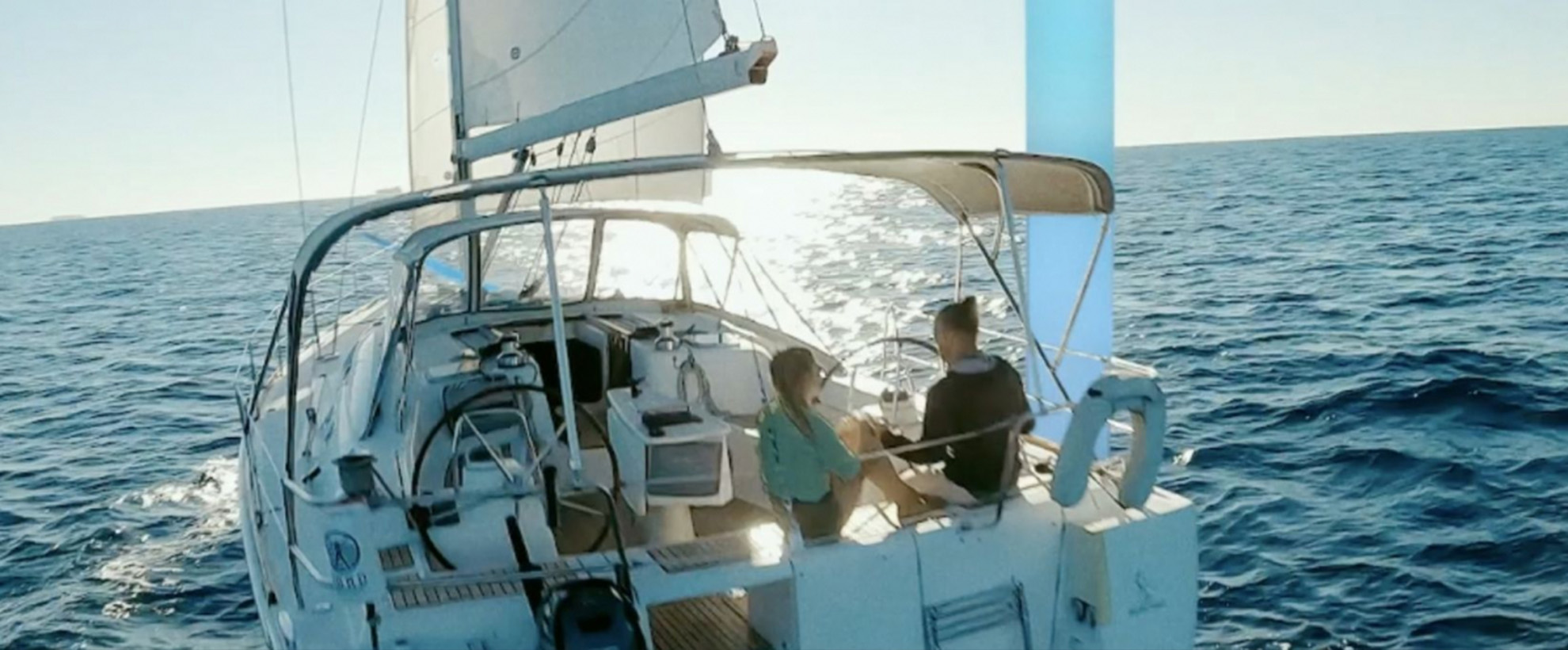 A man and a woman sit on a boat in the ocean with the sun gleaming on the water