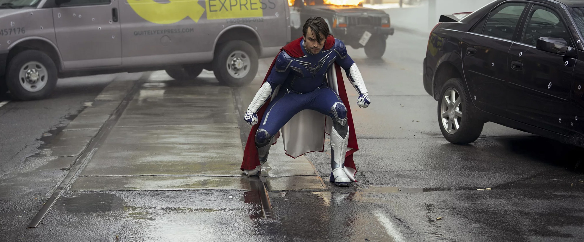 A young man in a superhero suit, lands on a busy street