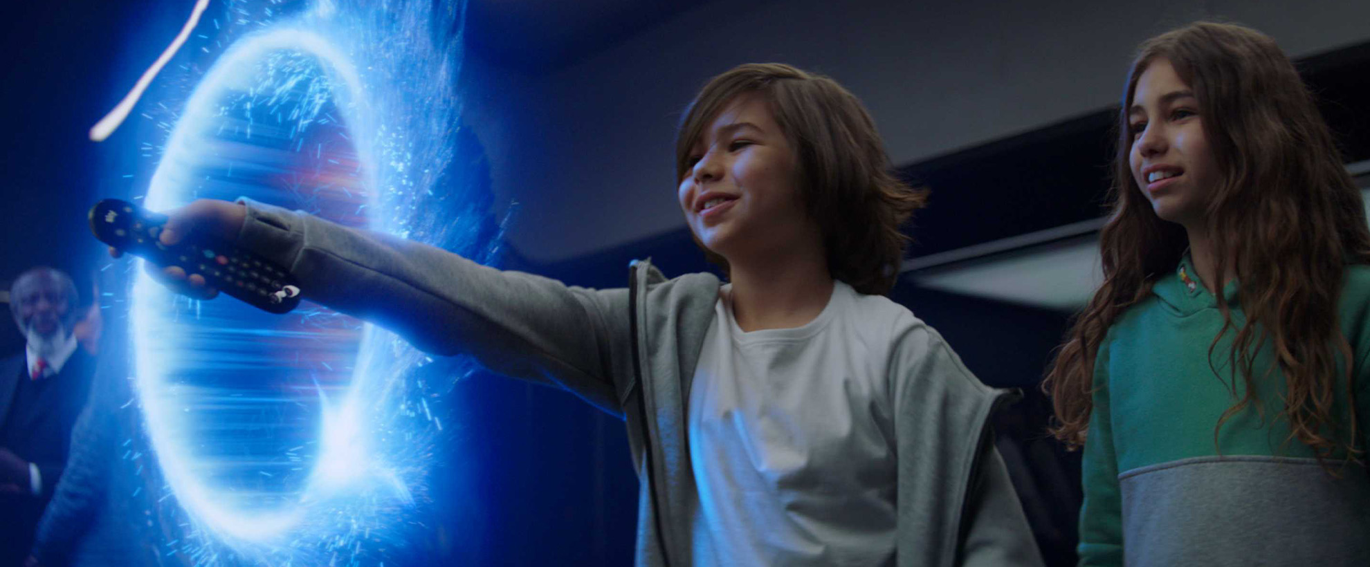 A young boy and a girl using a Sky TV remote, there is a glowing blue ring-shaped portal.