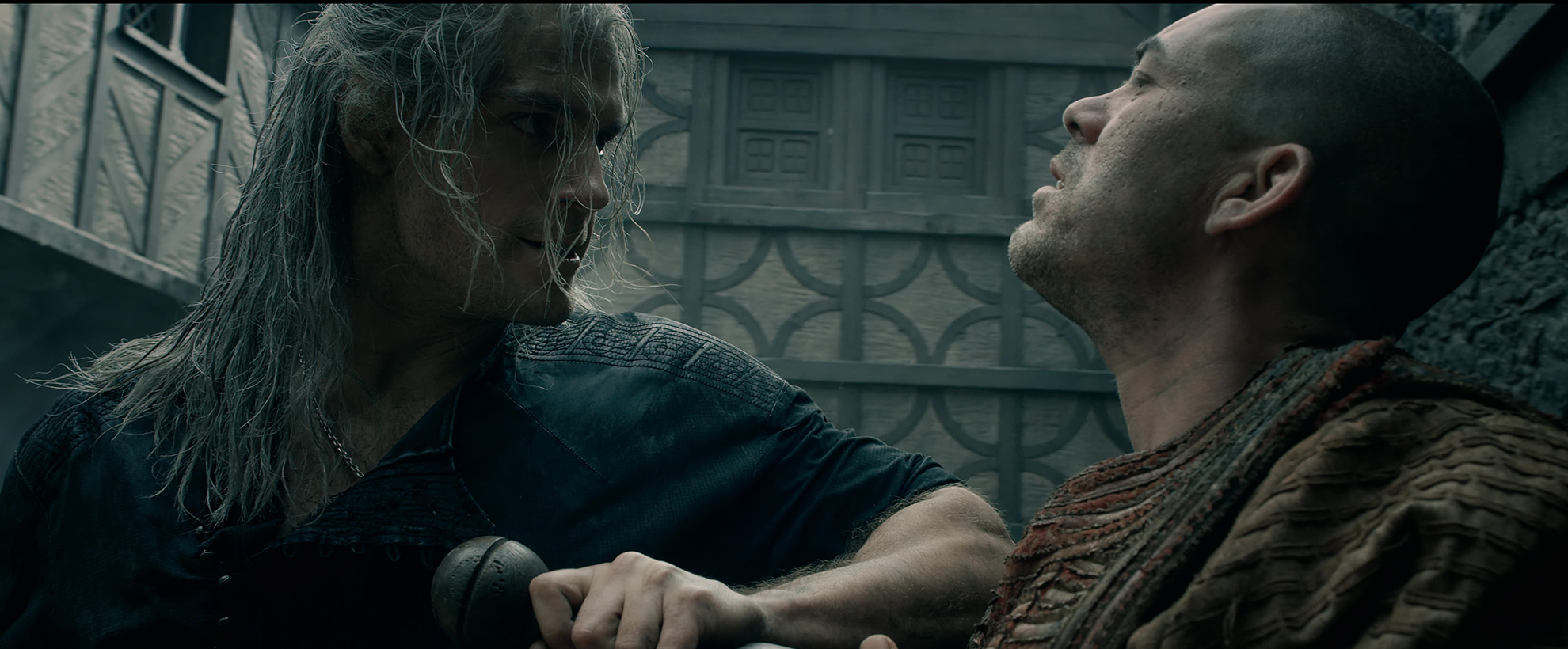 Henry Cavill holds a knife up to another man's chest in The Witcher