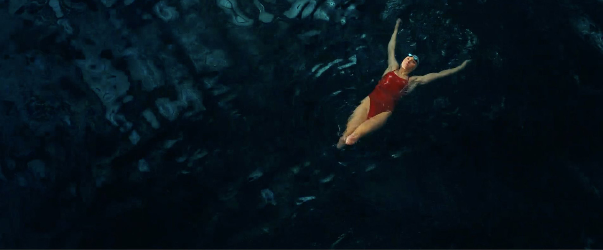 A female swimmer wearing red swimming on her back in dark water.