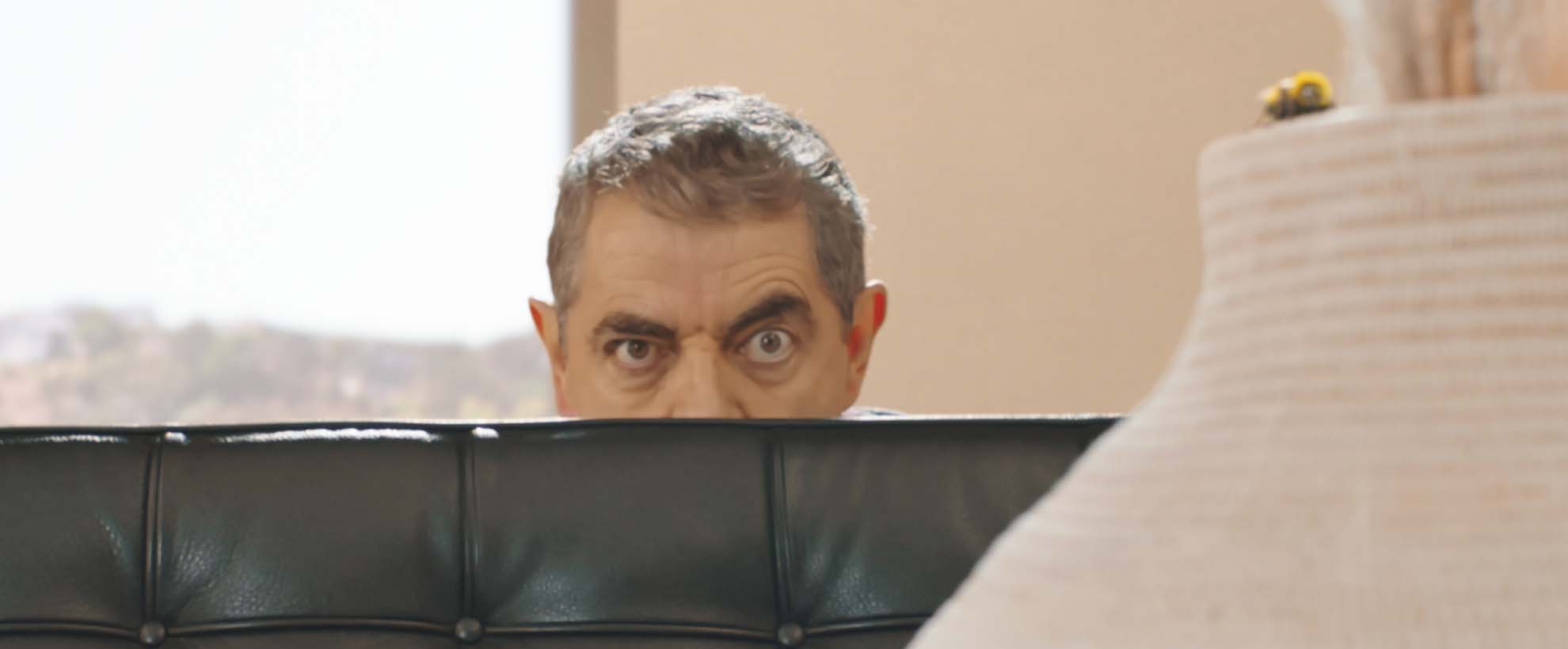 Actor Rowan Atkinson peers from behind a couch