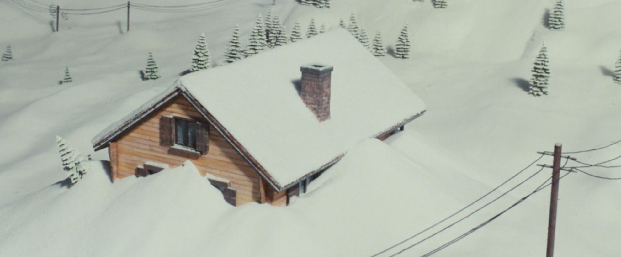 A cabin in the mountains is covered in snow from an avalanche.