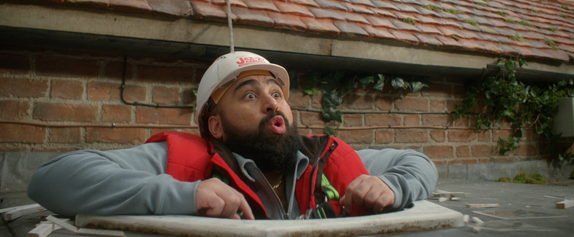 A Man wearing a hard hat is stuck in a hole in the roof.