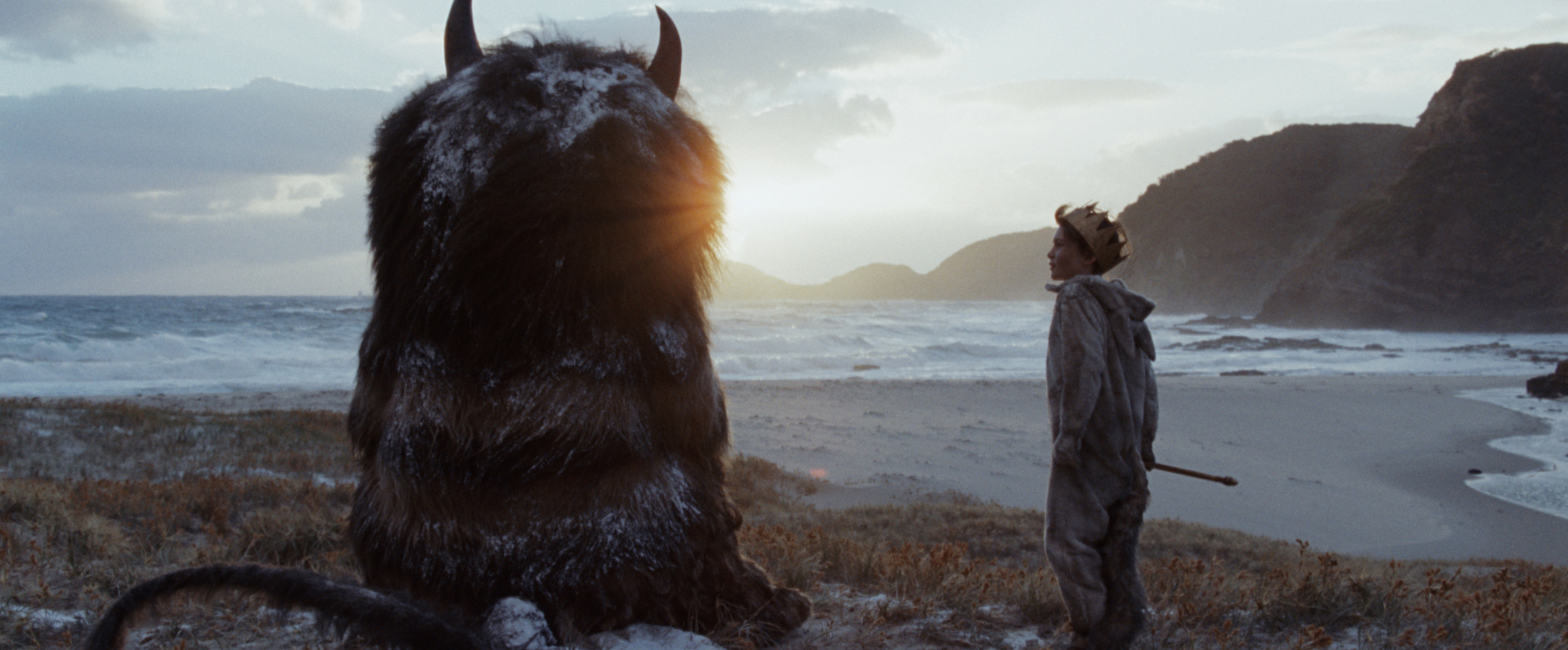 A young boy sits next to a large hairy creature with two horns