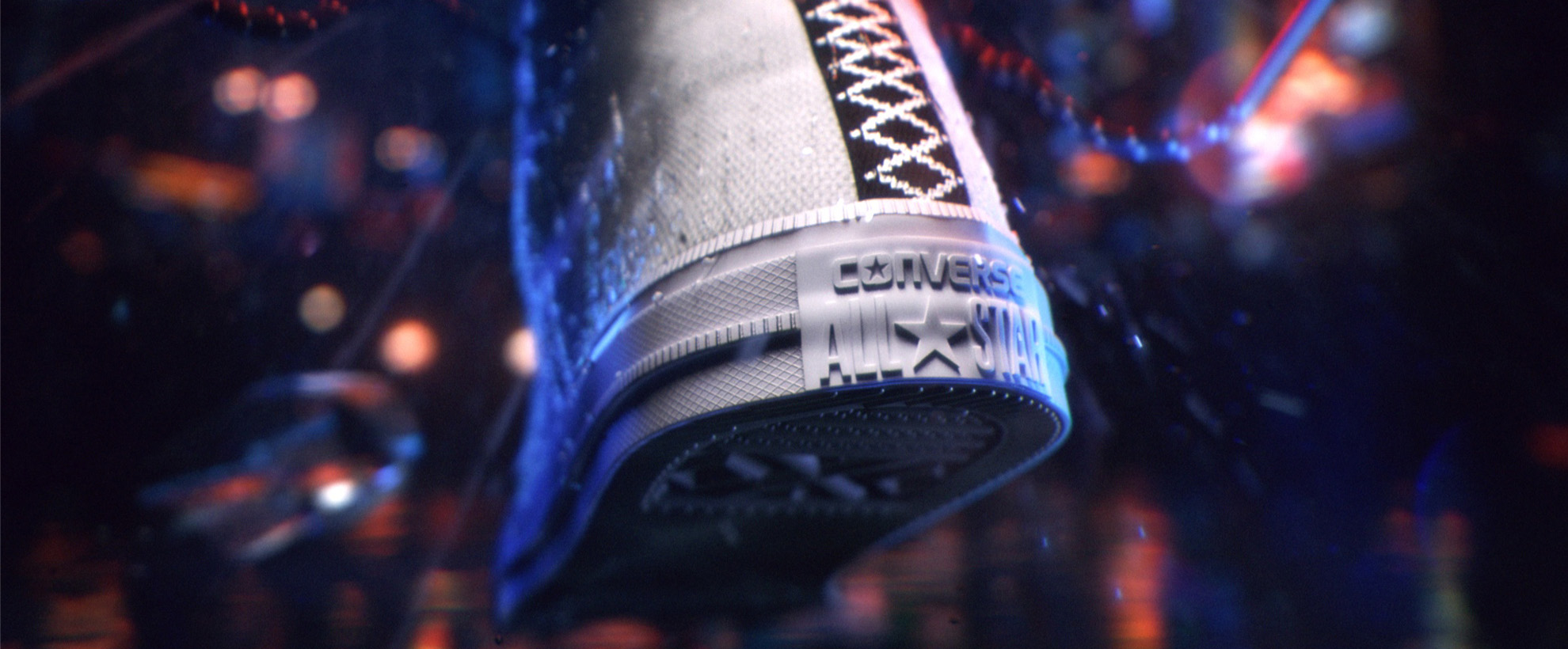 The back of a Converse trainer showing the logo and the underside of the shoe is splashing water. There are city lights in the background.