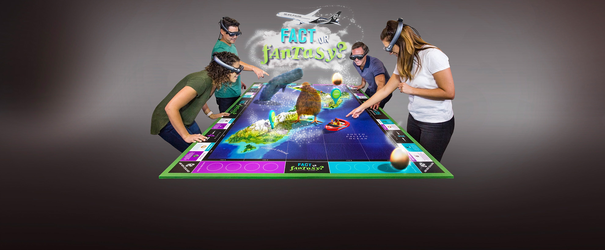 Two men and two women wearing VR goggles stand around a giant virtual board game that features the map of New Zealand