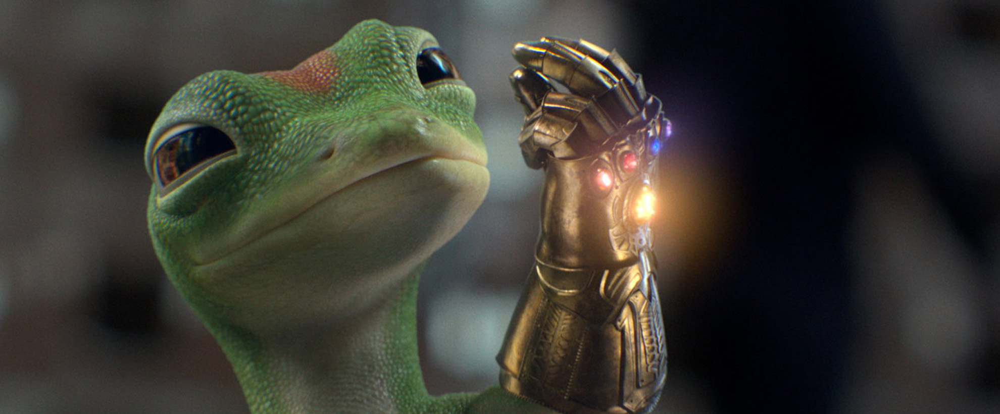 The GEICO gecko wears the Thanos gold armor glove with several different colored stones (aka Infinity Stones) 