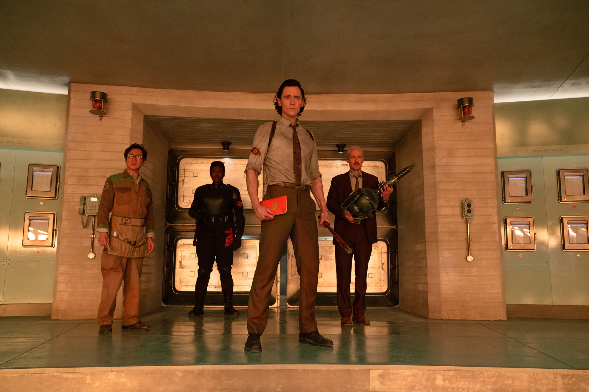 Loki and his friends at the TVA stand in a doorway, looking ahead