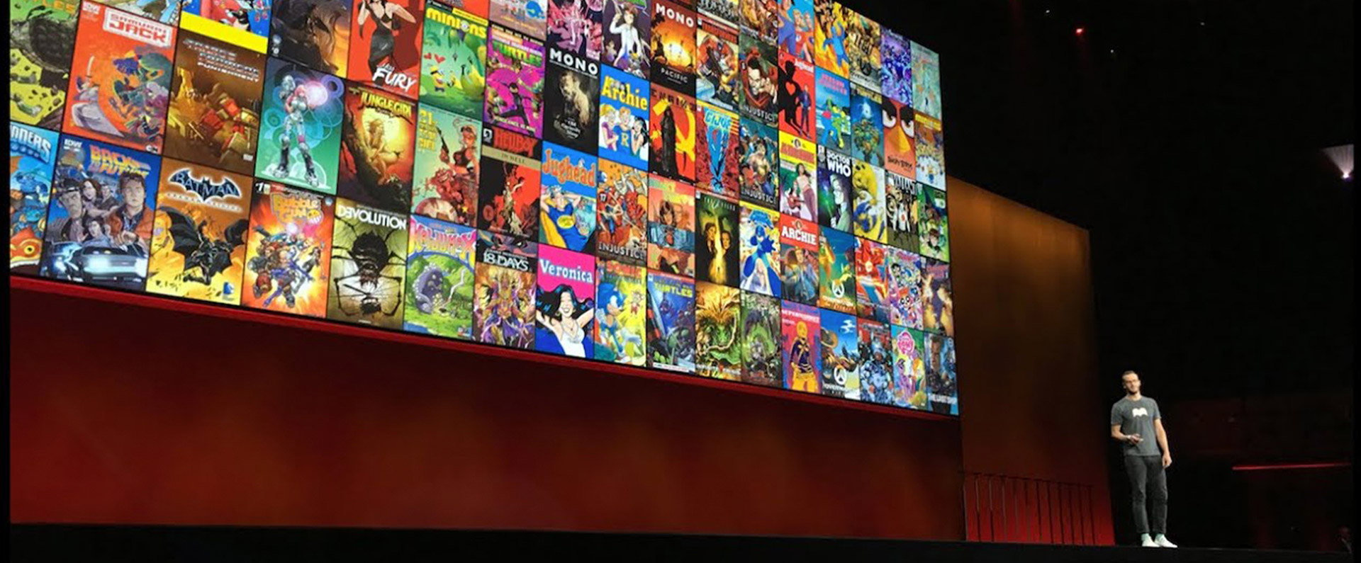 Man giving a talk on a stage in front of a wall of comic book covers