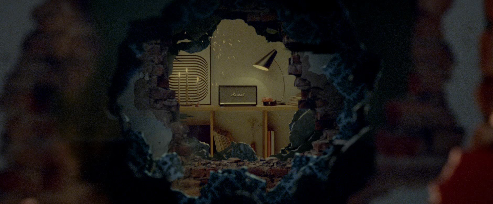 A partially destroyed wall shows a bedroom with a Marshall speaker sitting on top of a desk