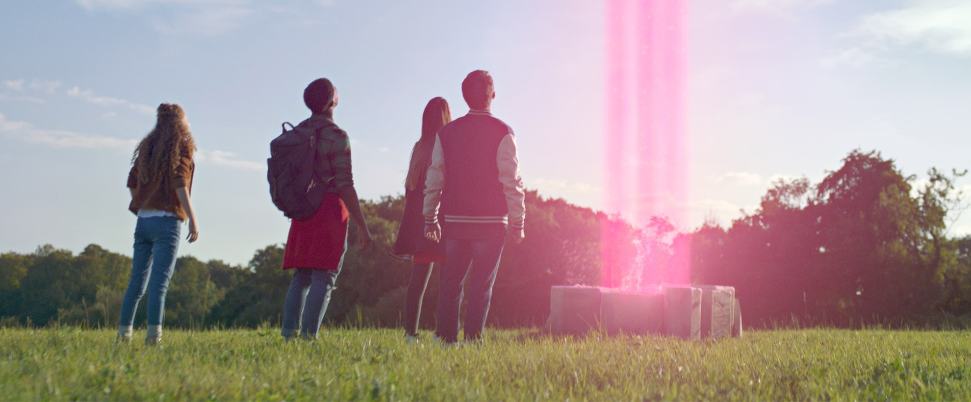 4 teens looking at a pink laser beam shooting into the sky