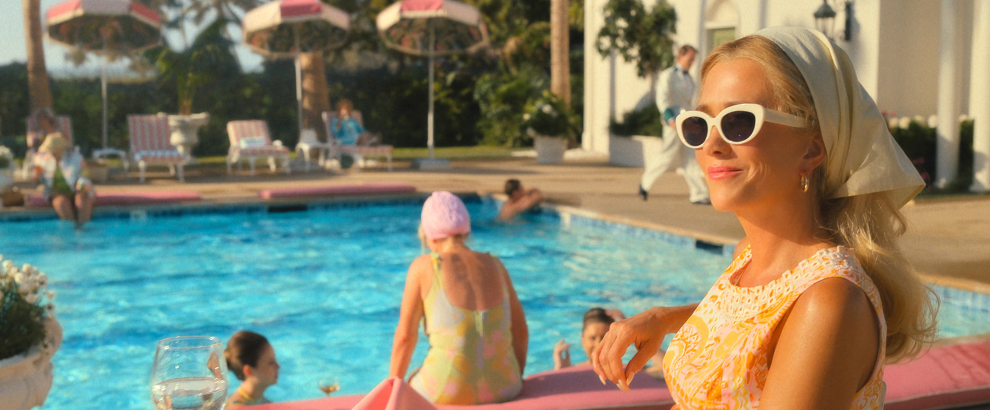 Kristen Wiig sits poolside in a 1960s holiday resort setting