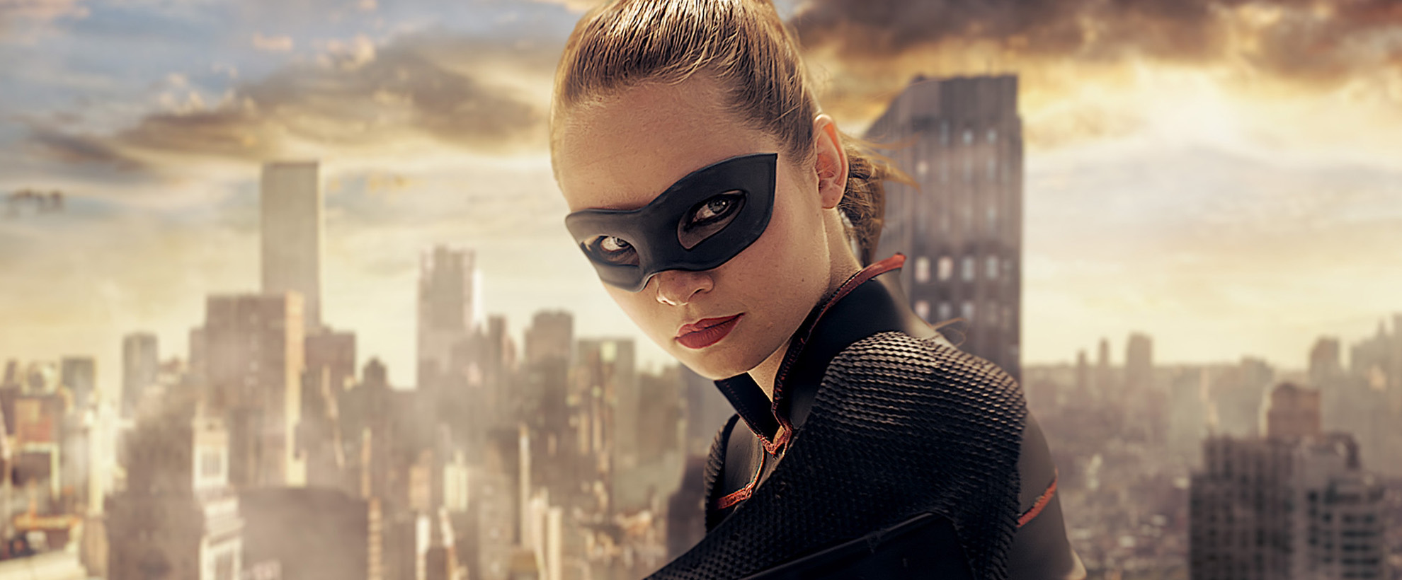 A woman with a superhero mask standing on the top of a building with a cityscape in the background.