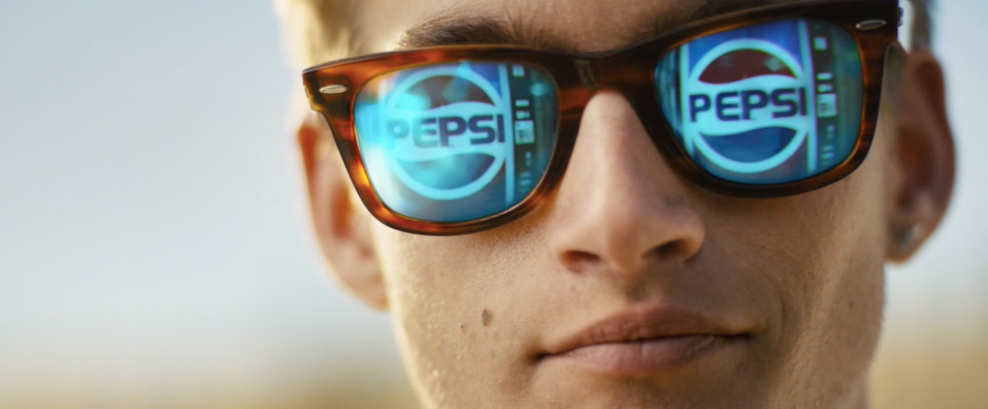 A blonde boy wears sunglasses with Pepsi in the reflection
