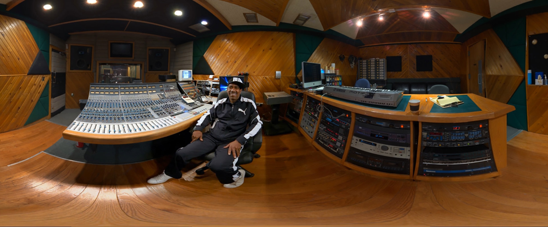 A fish-eye view of a man sitting at a mixing desk in a recording studio.