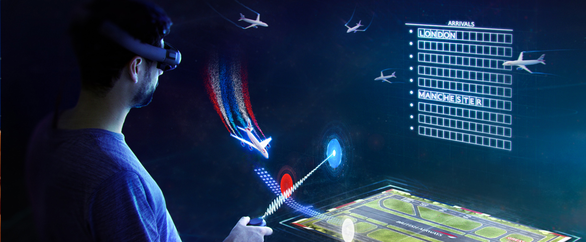 A man with a beard stands with VR goggles on. He is holidng a remote control that controls virtual planes. There are 5 virtual planes, with a virtual runway, and virtual arrivals & departures screen