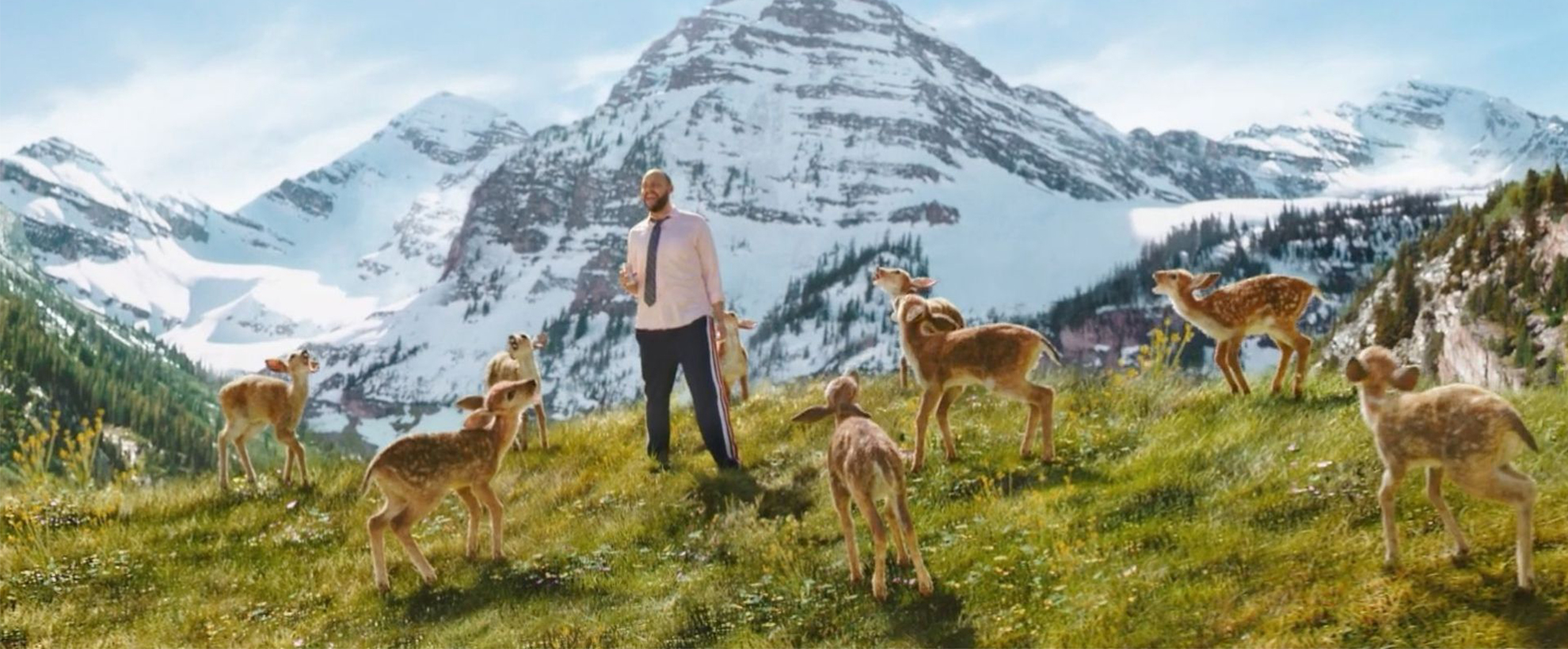 Man surrounded by dear standing in front of a mountain range