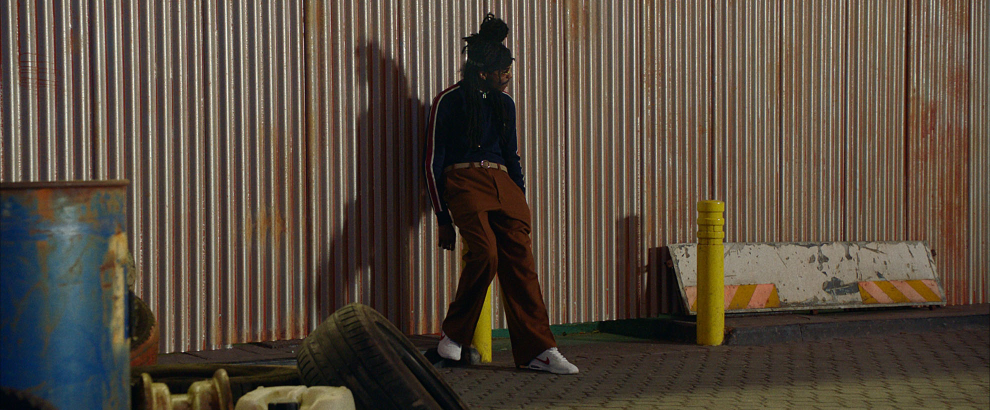 A man stands against a wall in an industrial part of town.