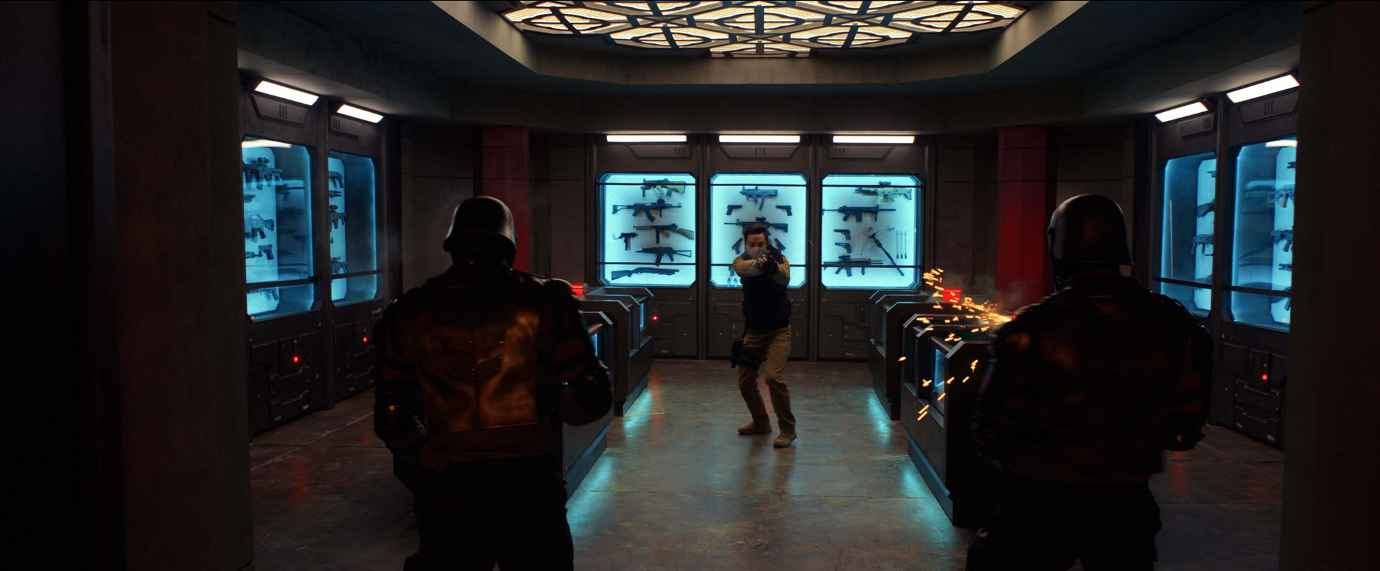 A man in body armour pointing a gun at two soldiers with their backs to the camera, there are many more weapons in cabinets behind the man.