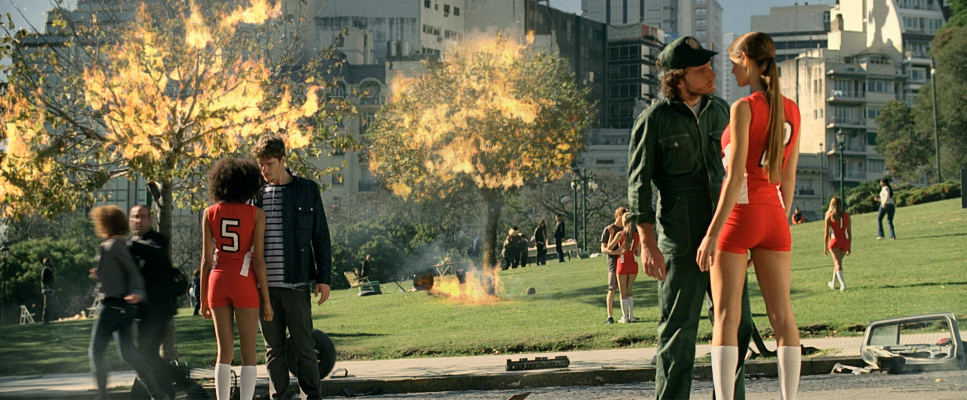 Trees are on fire as men and women stand in pairs of two staring at each other in a park.