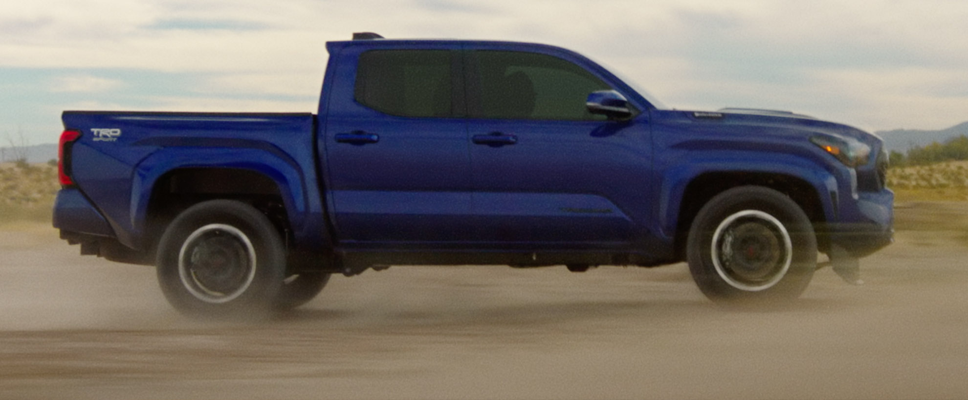 A blue Toyota Tacoma drives through the sand