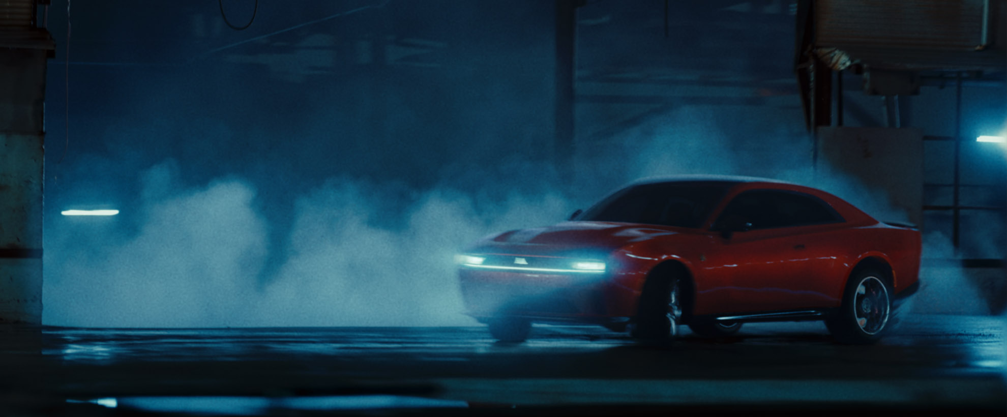 A red Dodge car drifts in an industrial parking lot