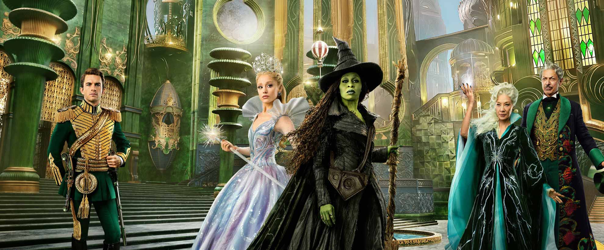 The cast of Wicked: For Good stand in costume in front of a CGI Emerald City. 