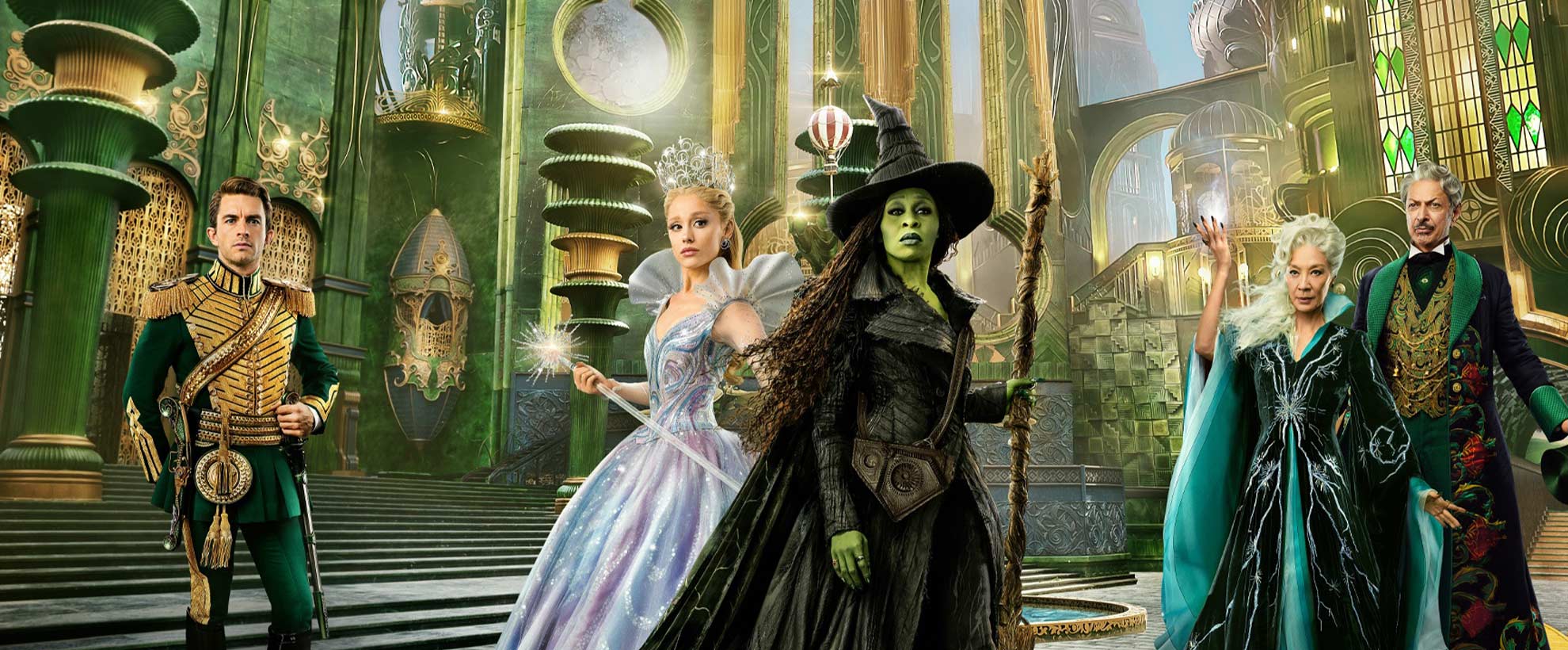 The cast of Wicked: For Good stand in costume in front of a CGI Emerald City.