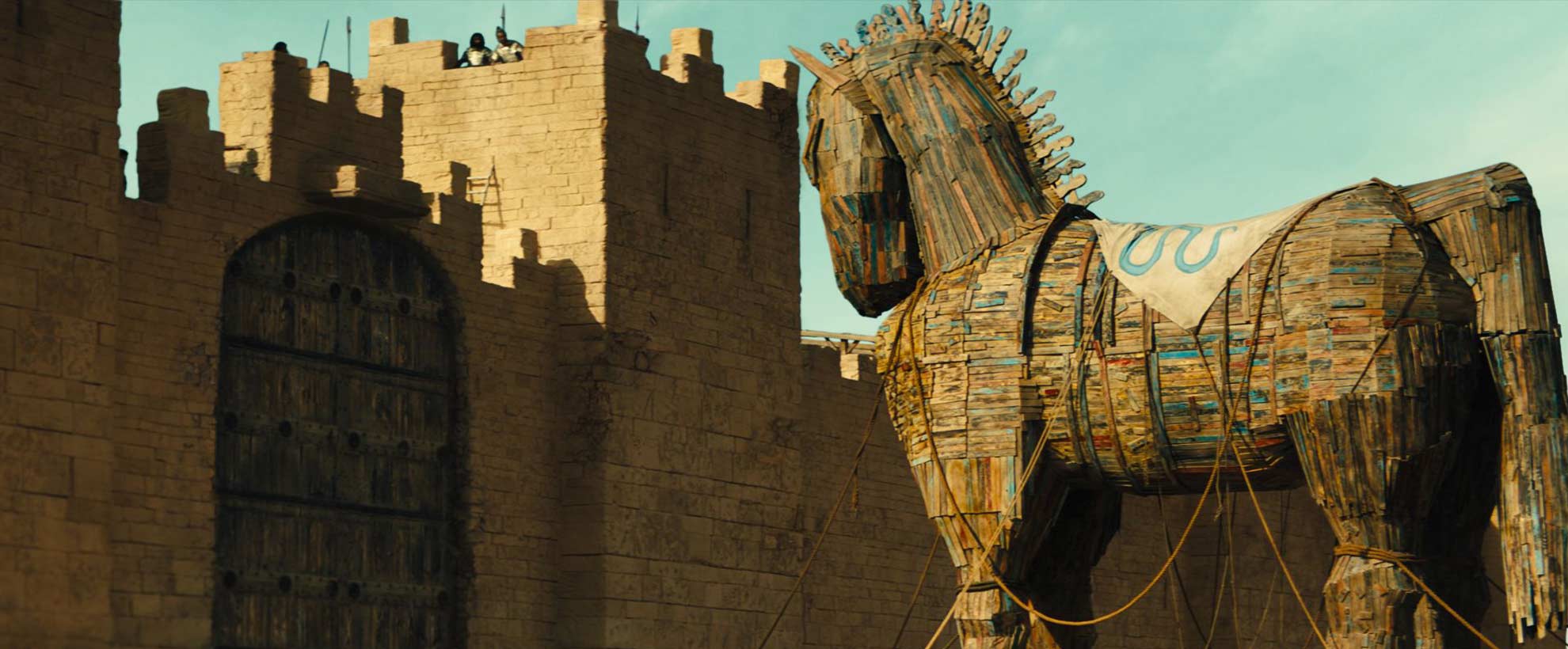 A large CGI trojan horse approaches a stone fortress