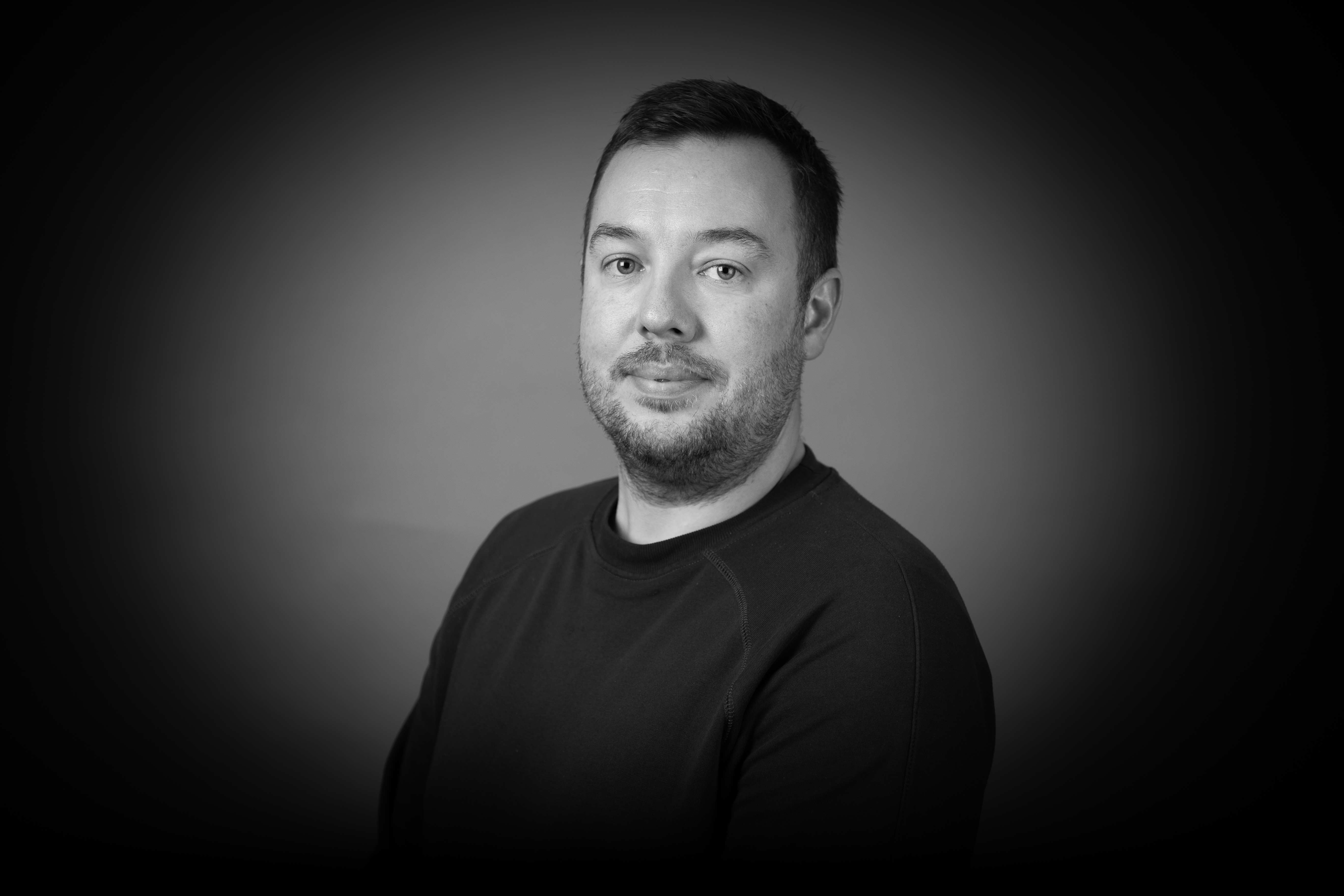 A black and white headshot of a white man against a grey background.
