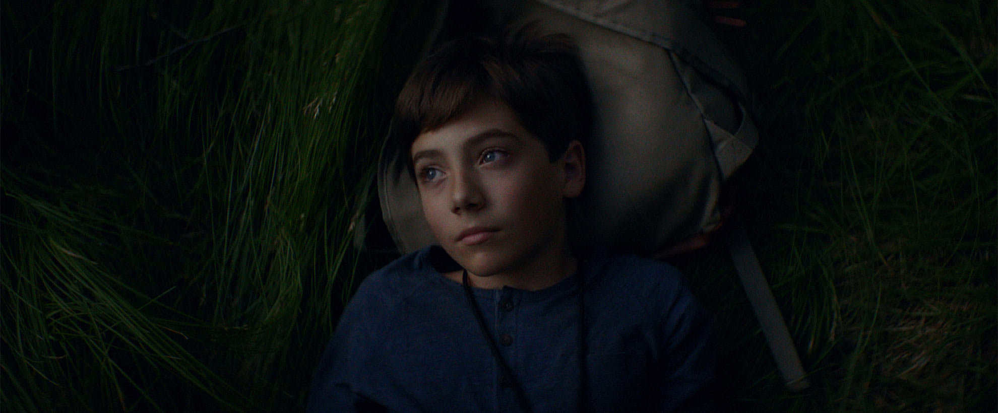 A kid lying on a bag in a green field