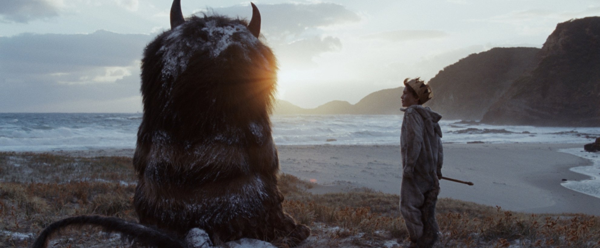 A young boy sits next to a large hairy creature with two horns