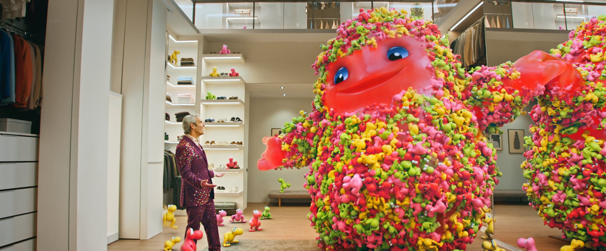 Andy Cohen stands in a large walk in closet with the CG animated Nerds Gummy Monster mascot
